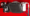Small cooling radiator with a white filter canister and metal piping mounted on a red panel, likely part of a vehicle’s fluid cooling system.
