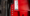 Close-up of red industrial equipment showing a vertical plate with a grease-point diagram and instruction labels, plus several silver bolts along the edge.