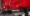 Close-up of a red agricultural machine with a large black discharge scoop and wheel assembly.