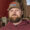 Bearded man in a brown cap with a blue logo, wearing a maroon hoodie, standing beside farm equipment outdoors.